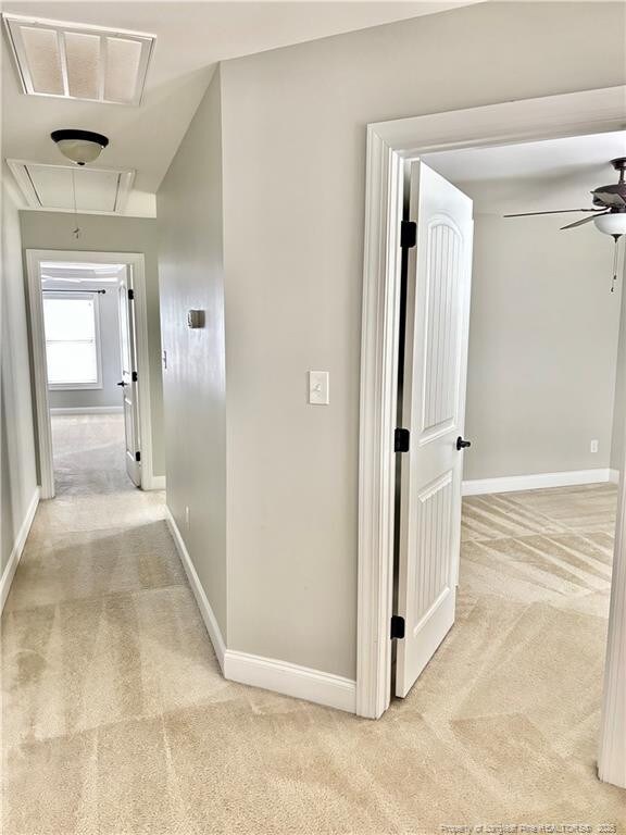 corridor featuring attic access, light colored carpet, visible vents, and baseboards