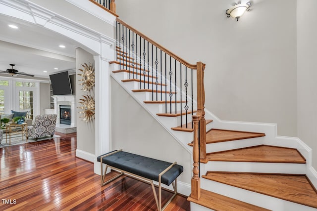 stairs featuring baseboards, a lit fireplace, a ceiling fan, and hardwood / wood-style flooring