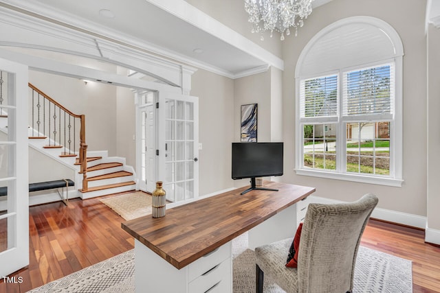 office space with a notable chandelier, crown molding, hardwood / wood-style flooring, baseboards, and ornate columns