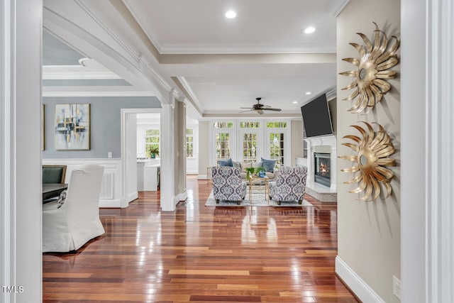 interior space with hardwood / wood-style floors, crown molding, a glass covered fireplace, and a ceiling fan