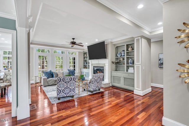 living room with crown molding, hardwood / wood-style flooring, a high end fireplace, visible vents, and ceiling fan