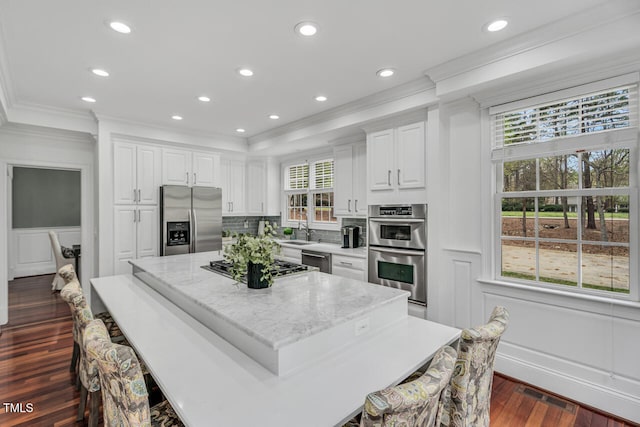 kitchen with crown molding, a kitchen island, white cabinetry, a decorative wall, and stainless steel appliances