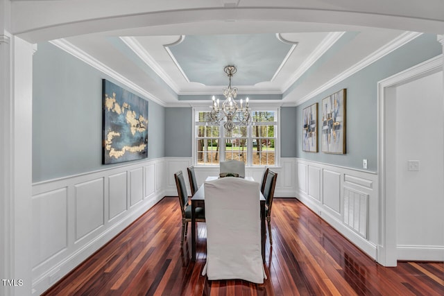 dining area featuring crown molding, an inviting chandelier, dark wood finished floors, a raised ceiling, and wainscoting