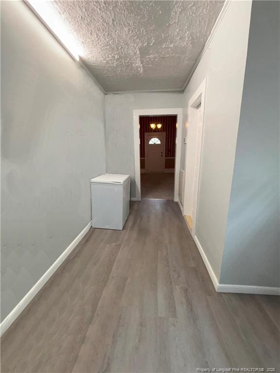 corridor featuring a textured ceiling, baseboards, and wood finished floors