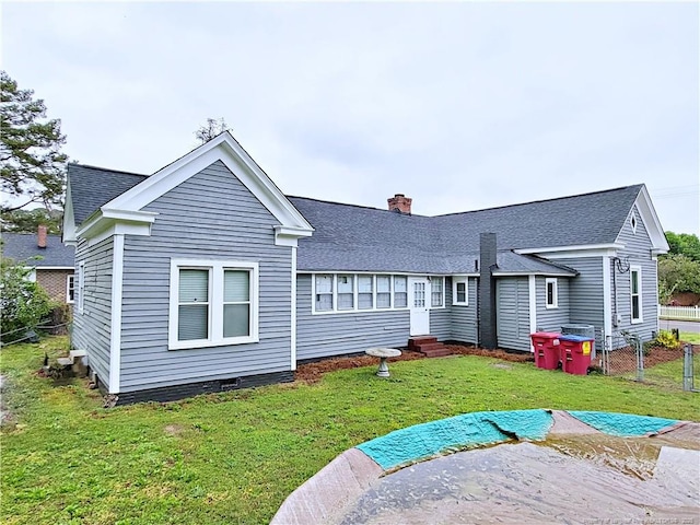 rear view of property featuring roof with shingles, a chimney, fence, entry steps, and a lawn