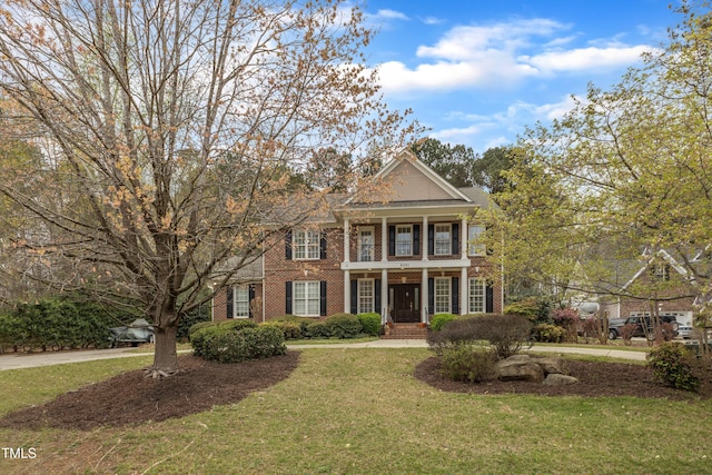neoclassical home with a balcony, a front yard, and brick siding