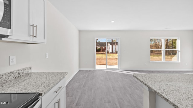 kitchen with stainless steel microwave, baseboards, light stone counters, white cabinets, and wood finished floors