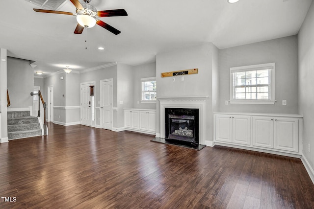 unfurnished living room with baseboards, ceiling fan, dark wood-style floors, stairway, and a glass covered fireplace