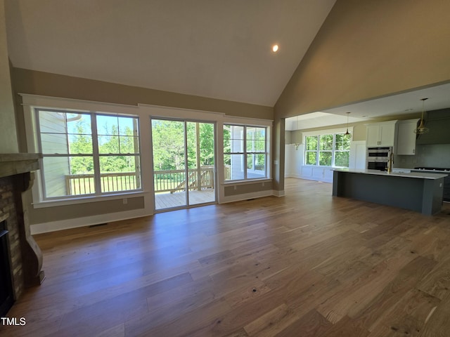 5480 Thom Rd, Mebane, NC 27302 - unfurnished living room featuring a sink, a fireplace, high vaulted ceiling, baseboards, and wood finished floors