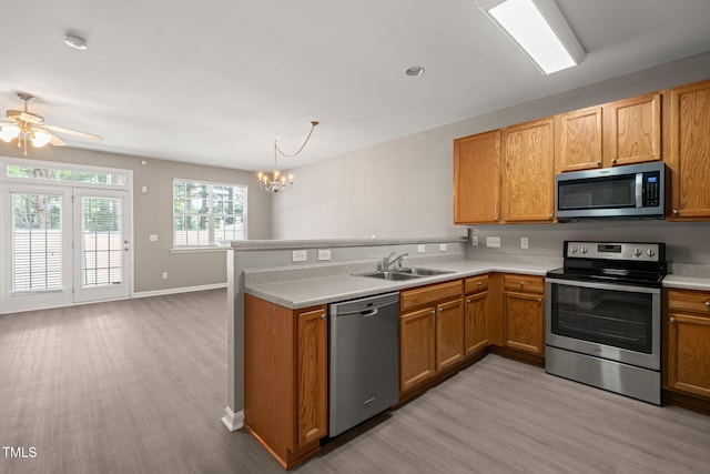 kitchen with stainless steel appliances, a sink, light wood-style flooring, a peninsula, and a chandelier