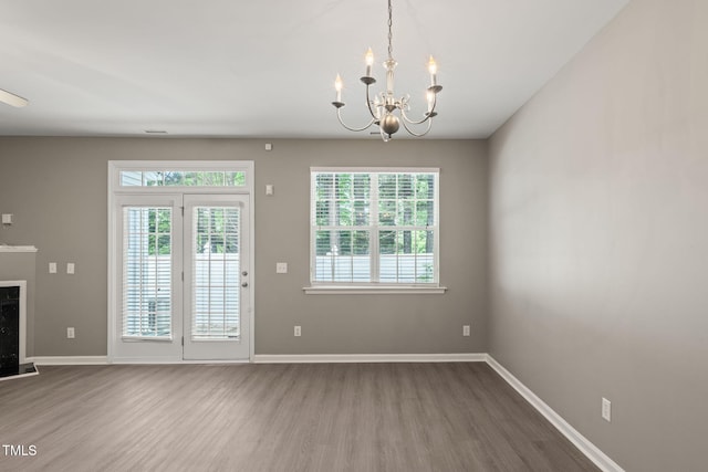 unfurnished dining area featuring wood finished floors, a chandelier, baseboards, and a fireplace