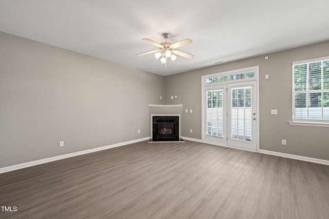 unfurnished living room featuring a ceiling fan, a high end fireplace, wood finished floors, and baseboards