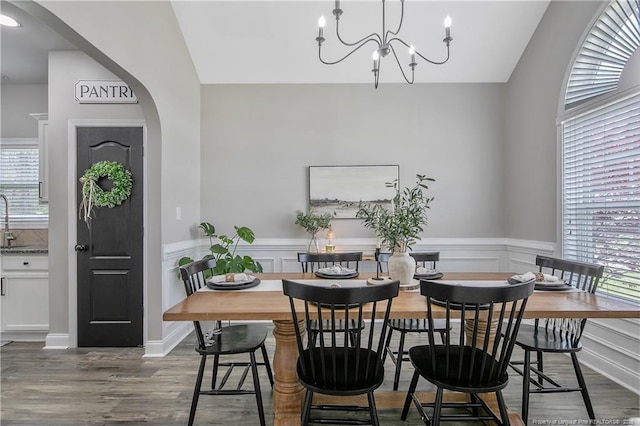 dining space with wood finished floors, a chandelier, arched walkways, a decorative wall, and wainscoting