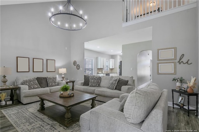 living room featuring a high ceiling, dark wood-style flooring, arched walkways, and a notable chandelier