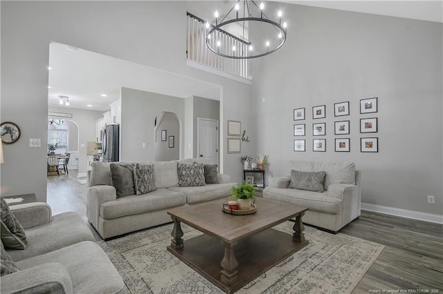living room featuring arched walkways, baseboards, wood finished floors, and a notable chandelier