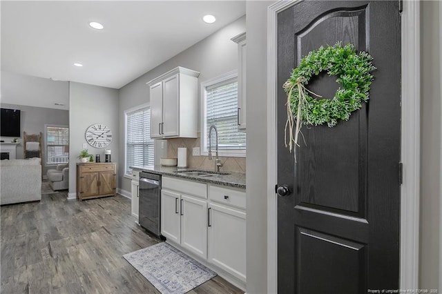 kitchen featuring light stone counters, a sink, wood finished floors, dishwasher, and decorative backsplash