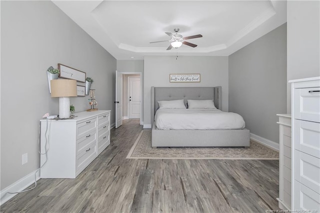 bedroom featuring a raised ceiling, baseboards, ceiling fan, and wood finished floors