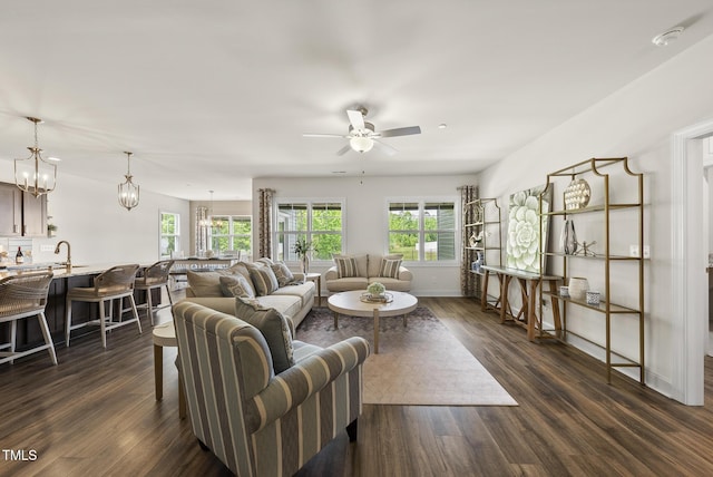 living area featuring dark wood finished floors, baseboards, and ceiling fan with notable chandelier