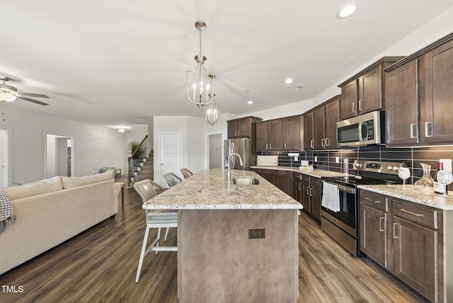 kitchen featuring a sink, a breakfast bar, stainless steel appliances, dark brown cabinetry, and open floor plan