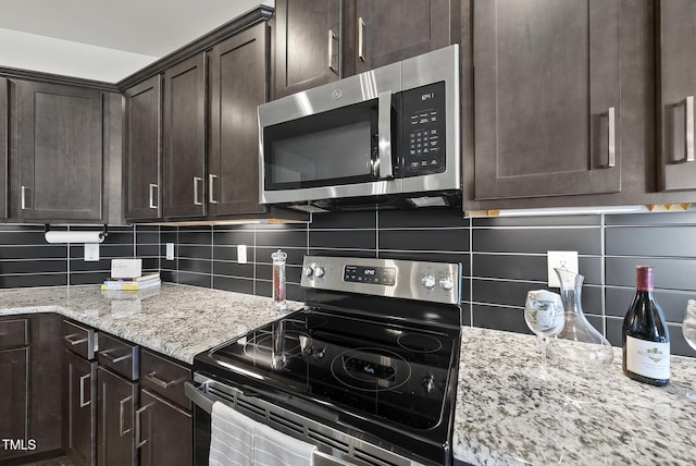 kitchen with dark brown cabinets, light stone countertops, stainless steel appliances, and backsplash