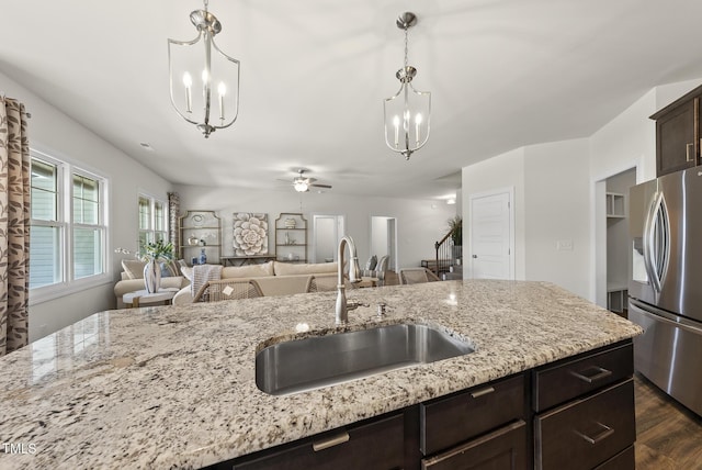 kitchen with a sink, stainless steel fridge, light stone counters, dark brown cabinets, and open floor plan