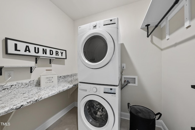 laundry room with stacked washer and clothes dryer, tile patterned flooring, laundry area, and baseboards