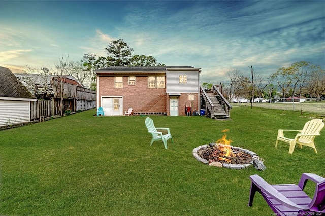 back of property with brick siding, a fire pit, stairway, and a yard