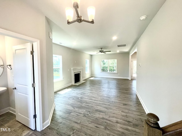unfurnished living room featuring visible vents, baseboards, a fireplace with raised hearth, wood finished floors, and ceiling fan with notable chandelier