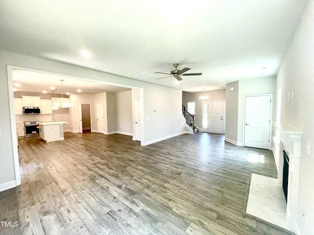 unfurnished living room with visible vents, ceiling fan with notable chandelier, stairway, a fireplace with flush hearth, and wood finished floors
