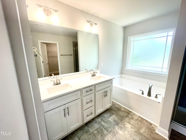 full bath featuring a garden tub, double vanity, a sink, and a spacious closet