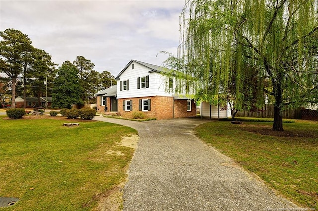 view of front of property featuring brick siding, aphalt driveway, fence, and a front lawn