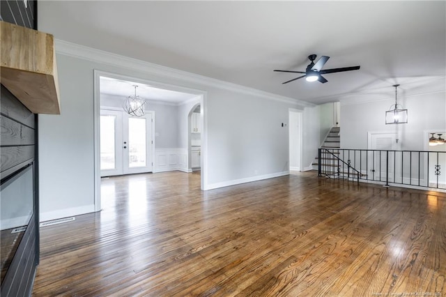 unfurnished living room with ceiling fan with notable chandelier, wood finished floors, ornamental molding, and stairs