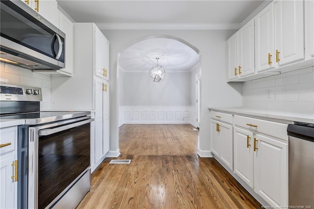 kitchen featuring white cabinets, visible vents, ornamental molding, appliances with stainless steel finishes, and arched walkways