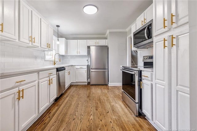 kitchen with tasteful backsplash, ornamental molding, white cabinets, appliances with stainless steel finishes, and wood finished floors