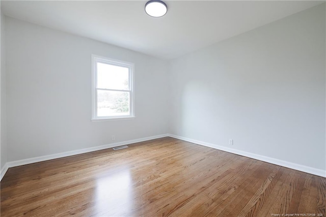 unfurnished room featuring baseboards, visible vents, and wood finished floors