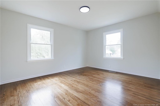 empty room with baseboards, visible vents, and wood finished floors