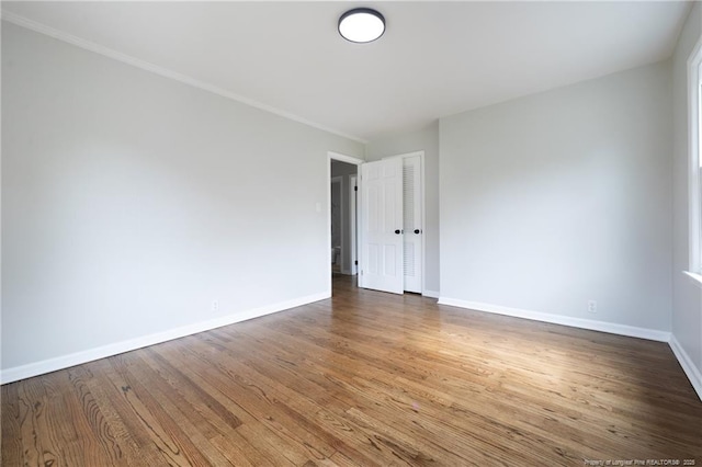 empty room with crown molding, baseboards, and wood finished floors