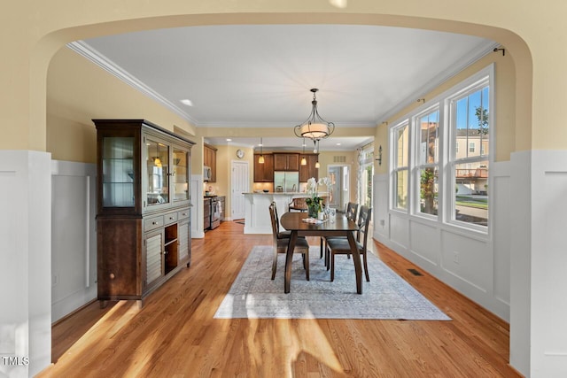 997 Windy Rd, Apex, NC 27502 - dining space featuring crown molding, light wood-style flooring, arched walkways, wainscoting, and a decorative wall
