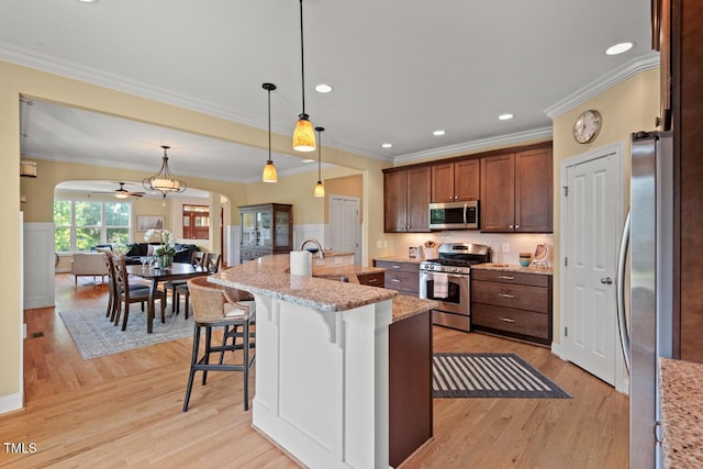 997 Windy Rd, Apex, NC 27502 - kitchen with appliances with stainless steel finishes, light wood finished floors, a breakfast bar, hanging light fixtures, and crown molding