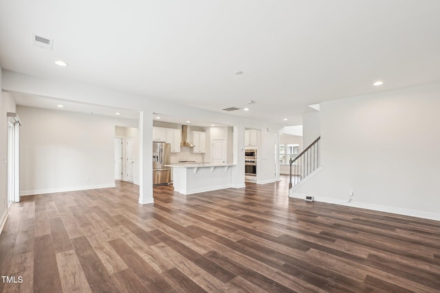 unfurnished living room featuring stairway, recessed lighting, baseboards, visible vents, and wood finished floors