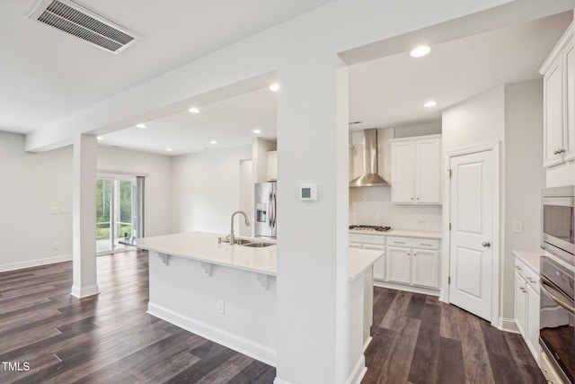 kitchen featuring dark wood-type flooring, a sink, visible vents, wall chimney range hood, and appliances with stainless steel finishes