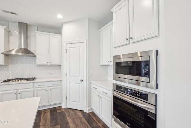 kitchen with tasteful backsplash, dark wood-style flooring, stainless steel appliances, white cabinets, and wall chimney exhaust hood