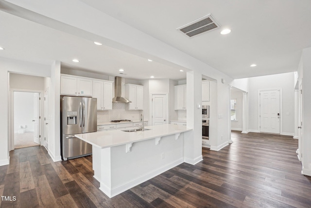 kitchen featuring light countertops, visible vents, appliances with stainless steel finishes, a sink, and wall chimney range hood