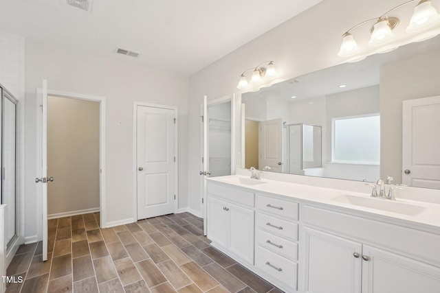 bathroom with a stall shower, double vanity, visible vents, and a sink