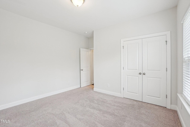 unfurnished bedroom featuring light colored carpet, a closet, and baseboards