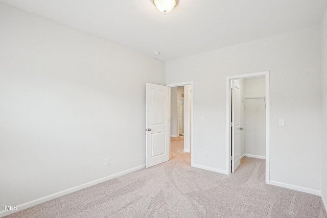 unfurnished bedroom with baseboards, a closet, a spacious closet, and light carpet