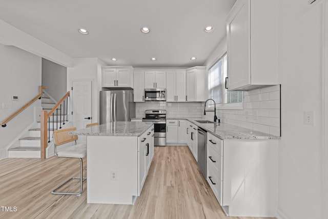 kitchen featuring light wood-style flooring, white cabinets, a center island, appliances with stainless steel finishes, and a sink