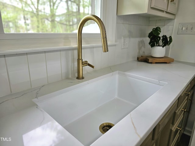 interior details featuring a sink, decorative backsplash, and light stone counters