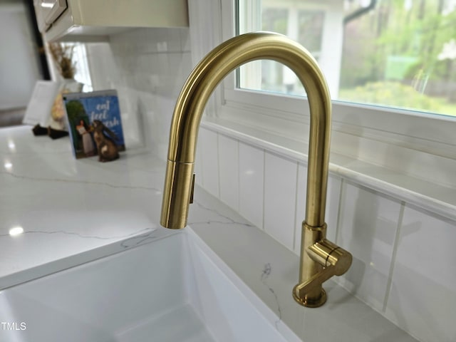 room details with a sink, white cabinetry, and light stone counters