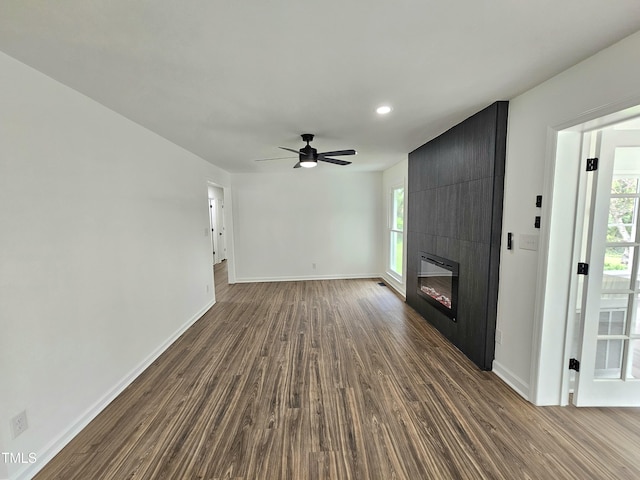 unfurnished living room featuring ceiling fan, a large fireplace, baseboards, and dark wood finished floors